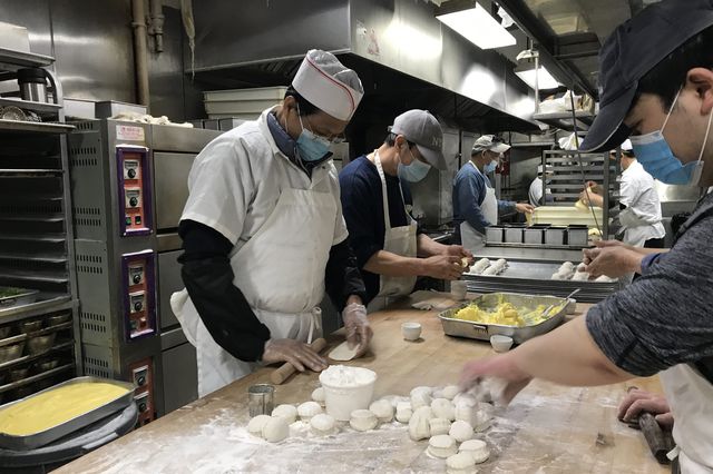 Shu Cheung Lai, wearing a mask, an apron, and cap, works in his bakery making bread with other workers